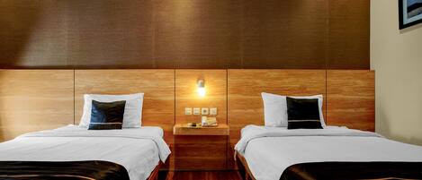 A hotel room with two beds, a wooden headboard, a nightstand with a lamp, and a wall-mounted picture.