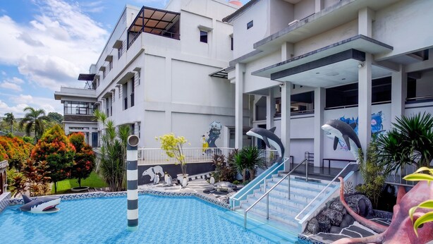 Una piscina con decorazioni a squalo e polpo, una zona esterna coperta e un edificio con balconi.