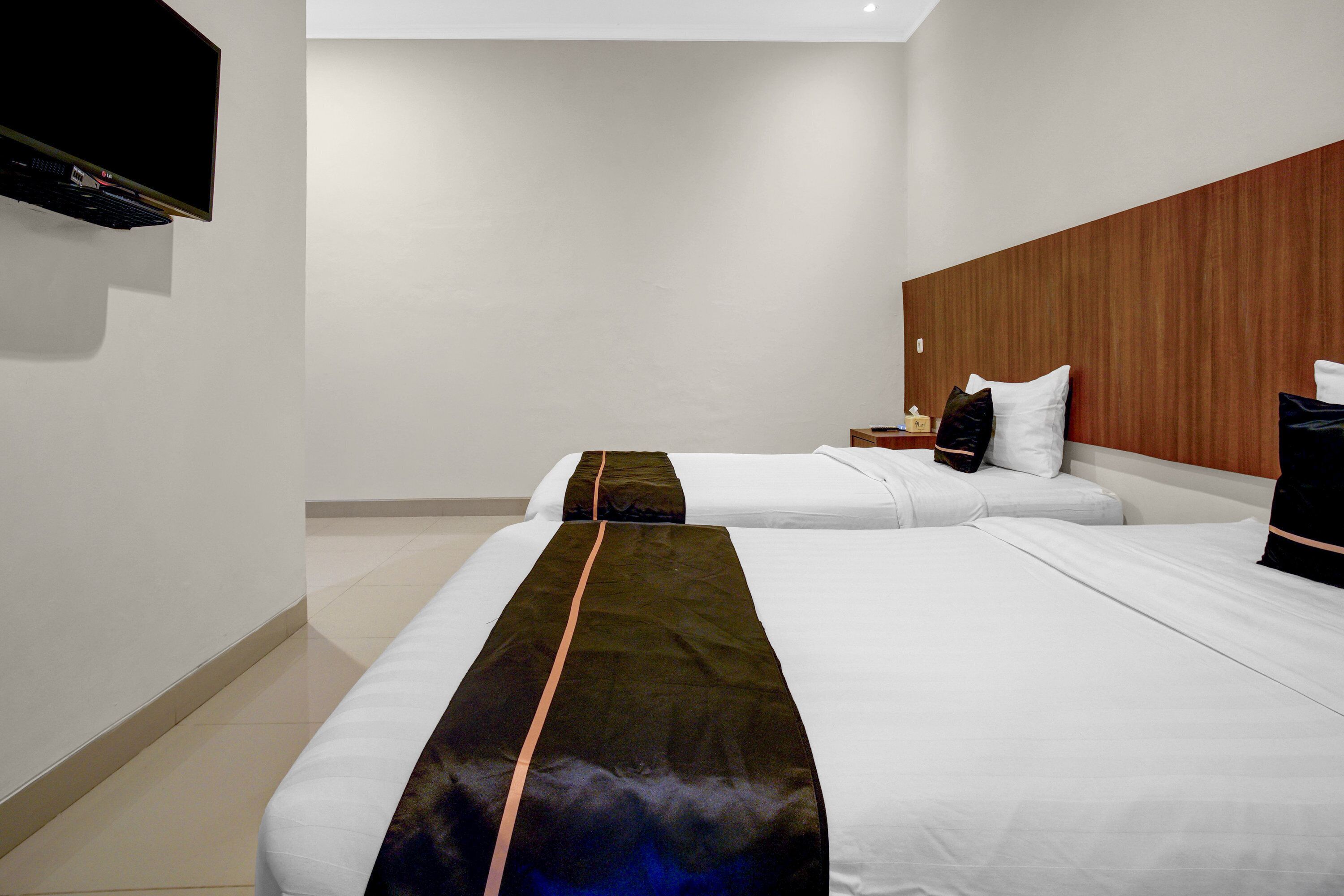 Ein Hotelzimmer mit zwei Betten, einem hölzernen Kopfteil, einem flachbildfernseher an der Wand und einem Nachttisch mit Lampe.