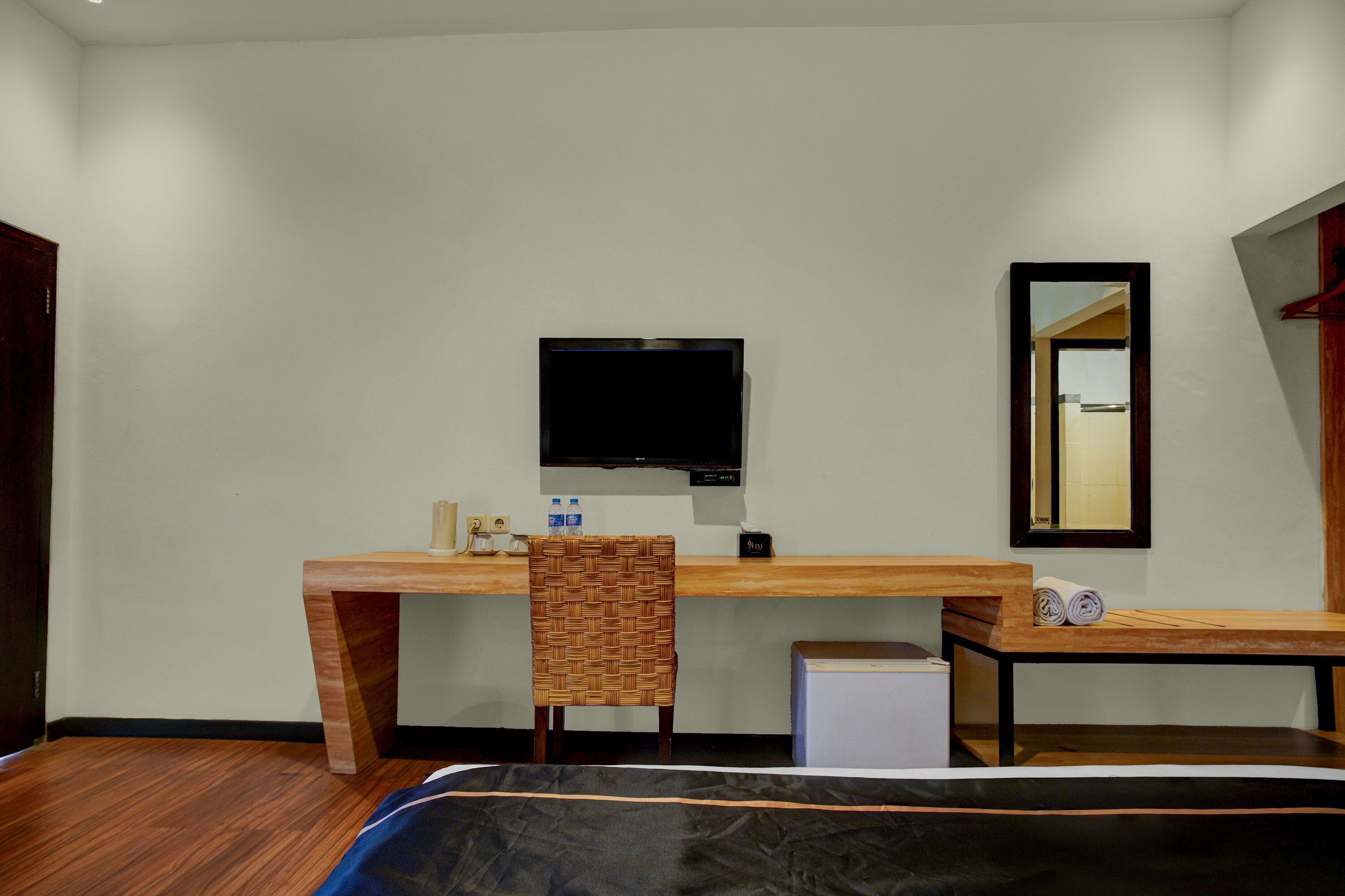 Une chambre d’hôtel avec un bureau en bois, un téléviseur fixé au mur, un miroir, un lit recouvert d’une courtepointe noire et bleue, et une petite armoire blanche.