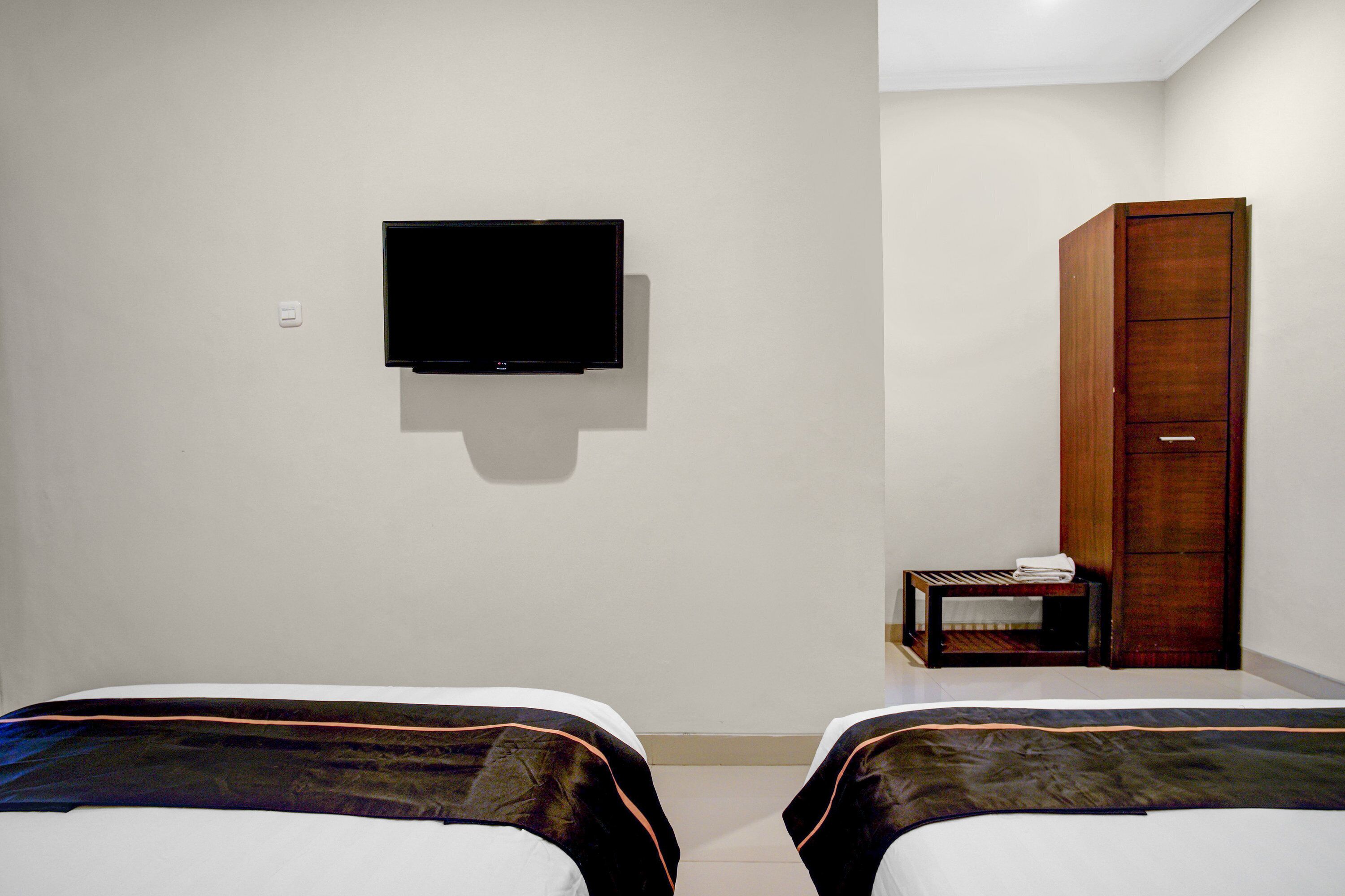 A hotel room with two beds, a television on the wall, and a wooden wardrobe.