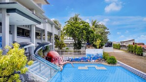 Una piscina con un affresco raffigurante un delfino, circondata da vegetazione e un edificio moderno.