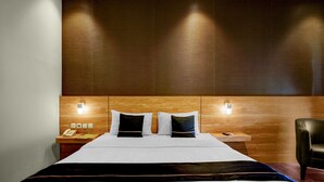 Una camera d'albergo con un letto grande, due comodini, una testiera in legno e una poltrona in pelle nera.