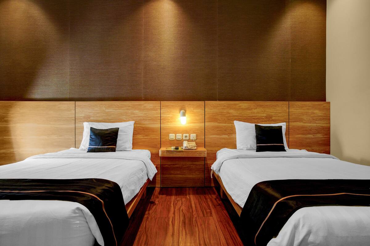 Une chambre d’hôtel avec deux lits, une tête de lit en bois, une table de chevet avec un téléphone et une lampe fixée au mur.
