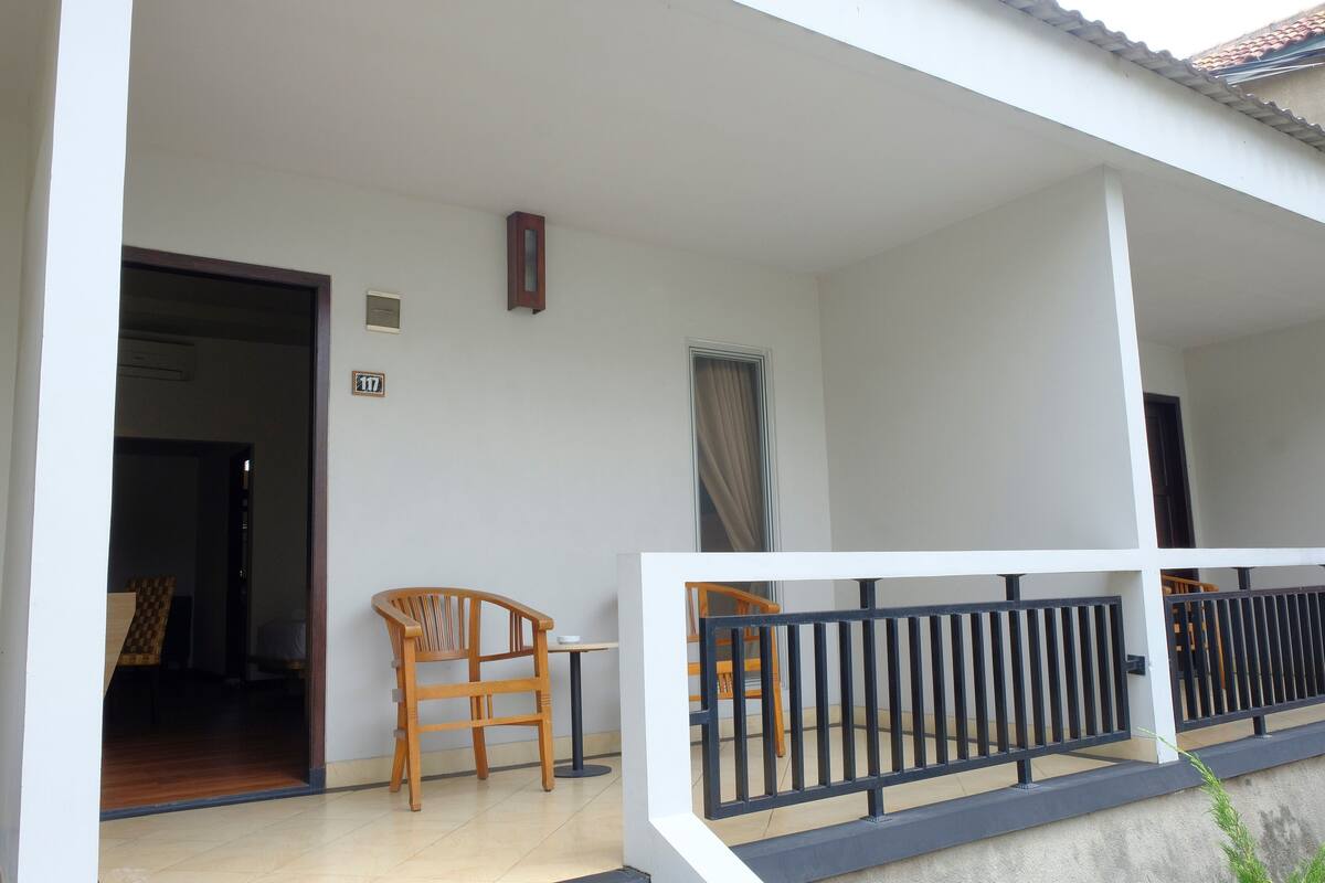 Un balcon avec une balustrade, une chaise en bois, une petite table et une porte donnant sur une pièce intérieure.