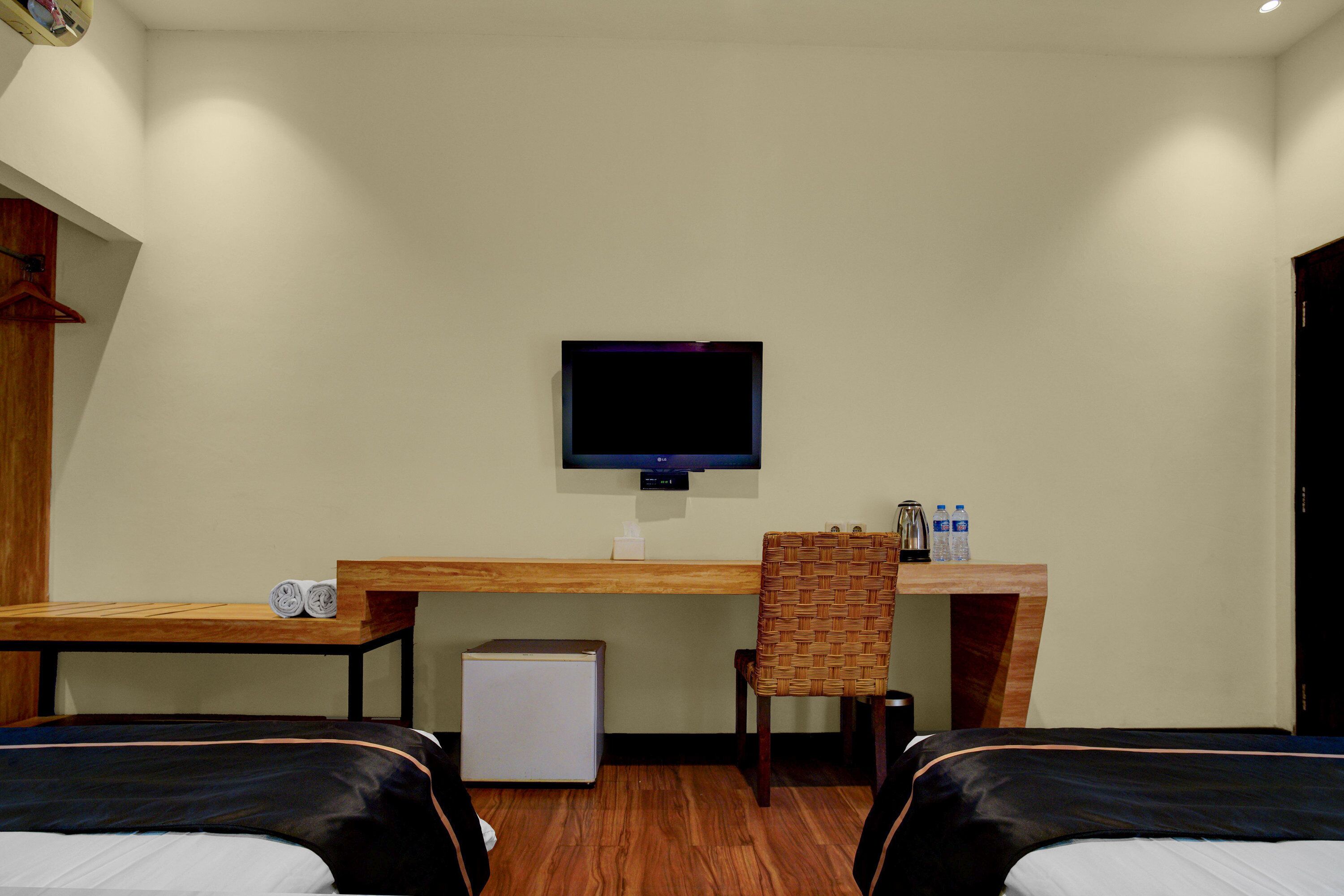A hotel room with two beds, a desk, a television, a small refrigerator, and a chair.