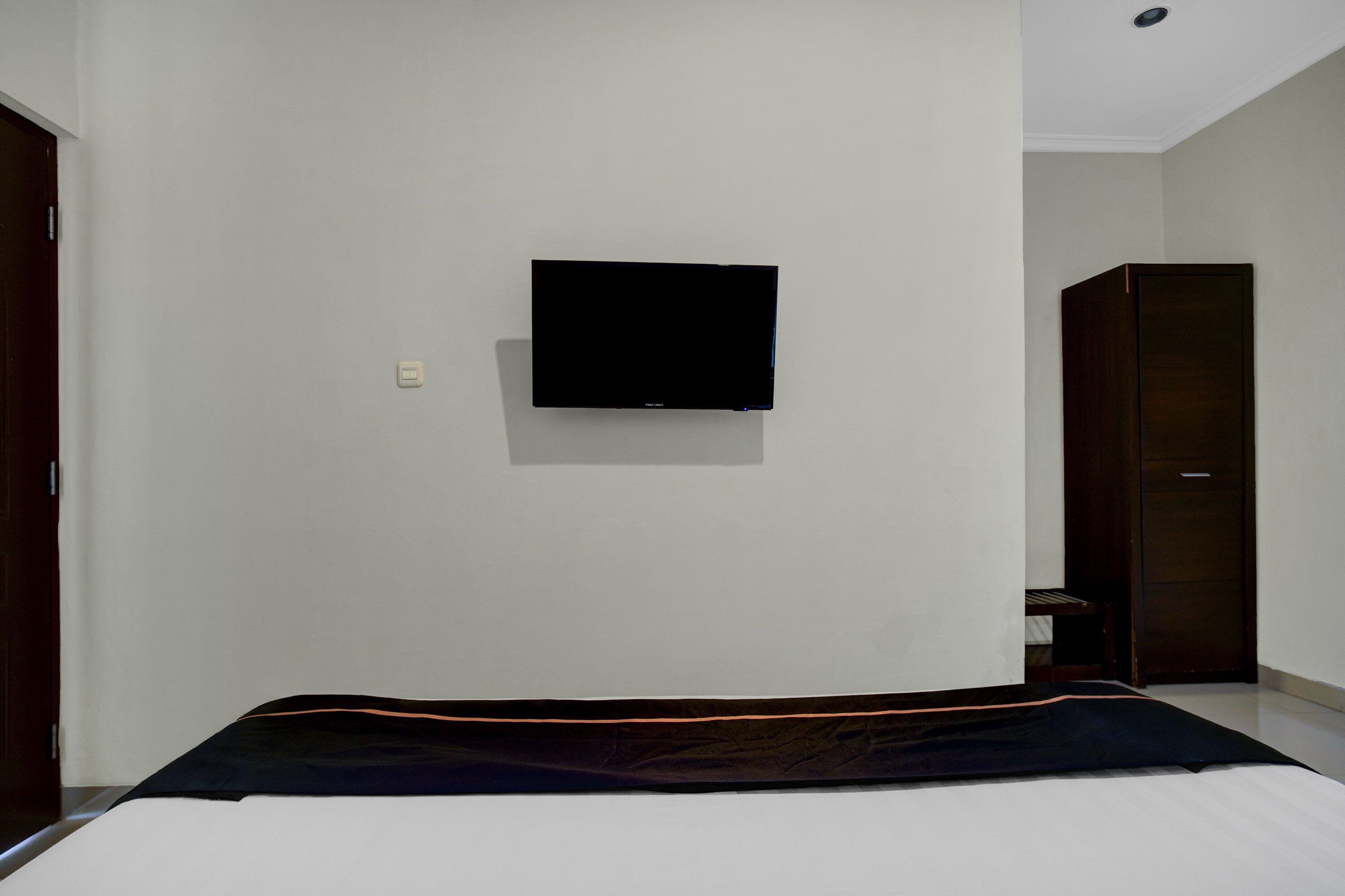Quarto com cama, televisão de tela plana na parede e porta que dá para outro cômodo.