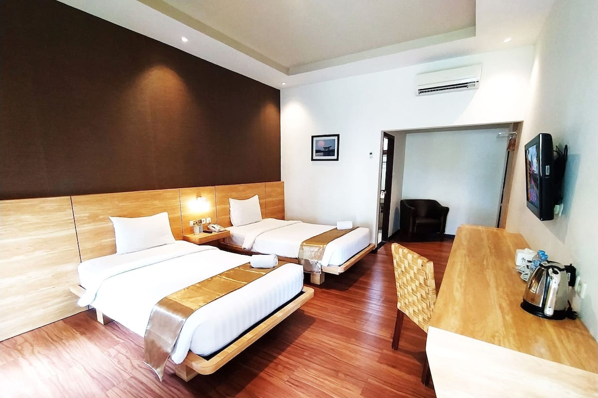 Une chambre d’hôtel avec deux lits, un bureau en bois, une chaise, une télévision et un appareil de climatisation.