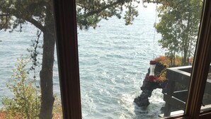 Una habitación con vistas a un lago a través de una ventana, una mesa de madera con un posavasos y una taza, y una silla.
