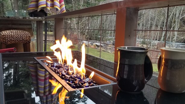 A glass-top table with a tray of burning wood, a black mug, and a striped container.