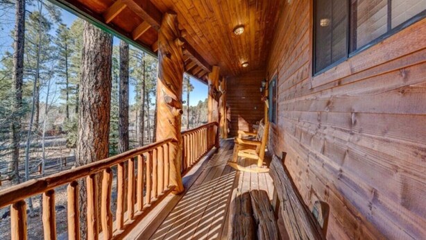 A wooden cabin with a covered porch, large windows, and a view of the surrounding forest. - Huge Cabin Near Woodland Lake, Sleeps 36! (Pinetop-Lakeside)