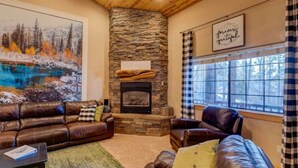A cozy living room with a stone fireplace, leather sofas, and a large painting of a winter landscape. - Huge Cabin Near Woodland Lake, Sleeps 36! (Pinetop-Lakeside)