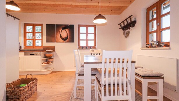 Une cuisine chaleureuse avec des meubles en bois, une table à manger entourée de chaises blanches et un panier en osier posé sur le sol.
