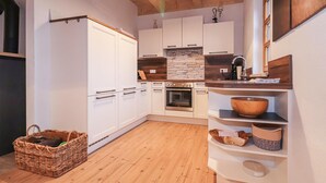 Une cuisine avec des armoires blanches, un pare-feu en pierre, un plan de travail en bois et un panier posé sur le sol.