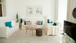 Een moderne woonkamer met een witte bank, een salontafel, een tv op een glazen voetstuk en twee ingelijste foto's aan de muur.