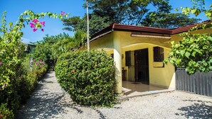 A yellow building with a red roof, surrounded by greenery and a gravel path. - Tropical Patio & Garden, Walk to Samara Beach
 (Sámara)