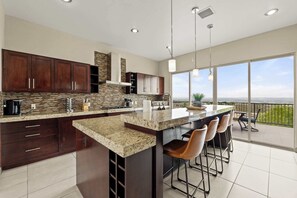 A modern kitchen with a large island, dark wood cabinets, and a view of the ocean. - Mountain View Pool House (El Paso)