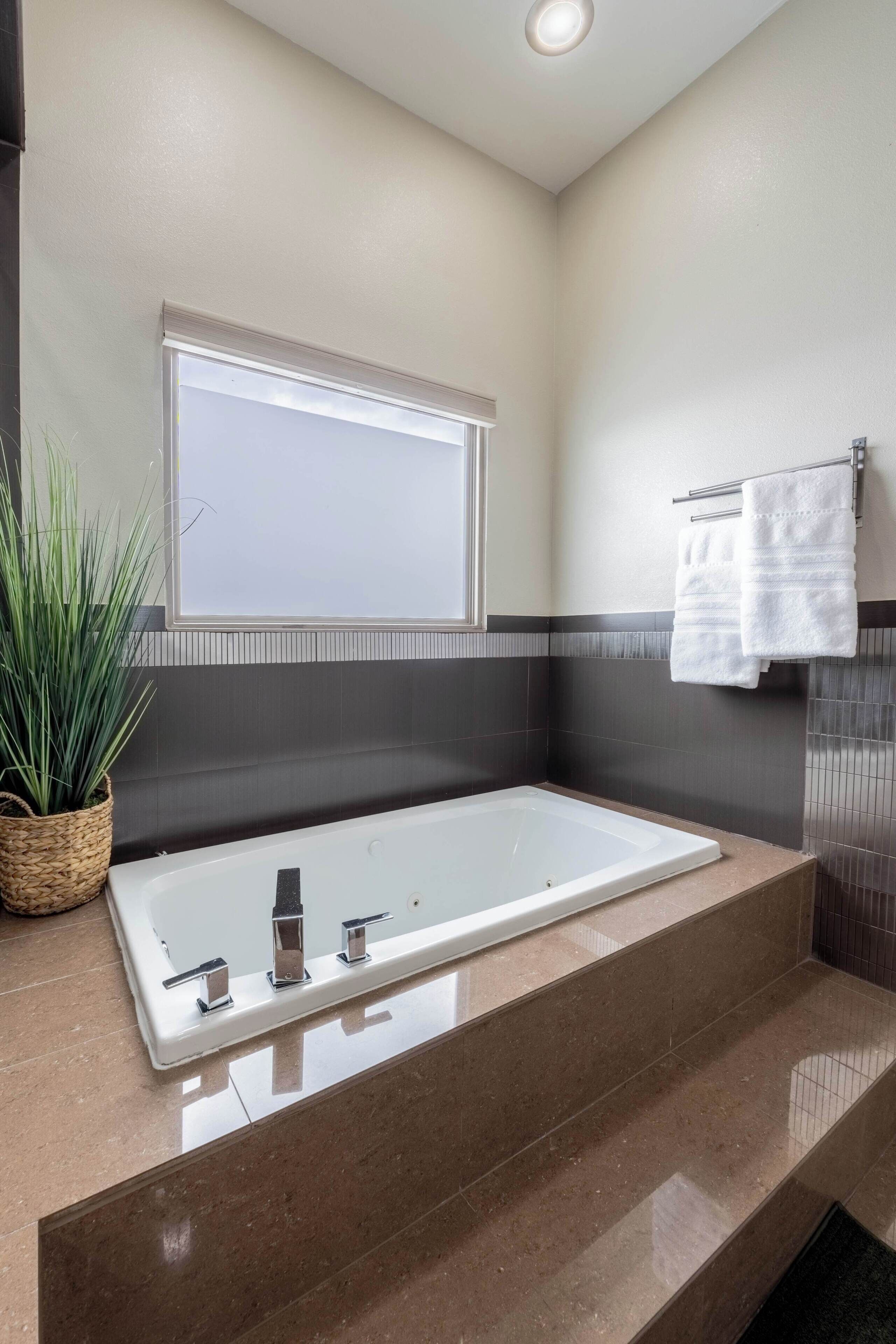 Un baño con una bañera grande, una planta en maceta y un perchero para toallas.