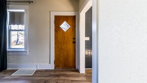 A room with a wooden door, a window with a view, and a vent on the floor.