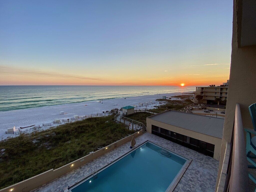 Un espace piscine offrant une vue sur la plage et l’océan au coucher du soleil.