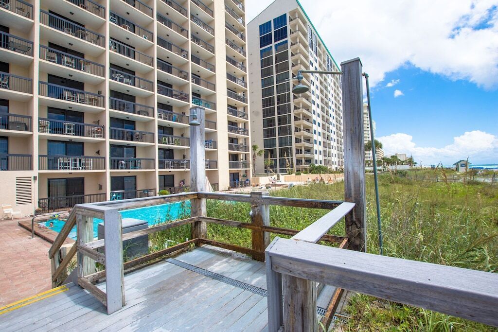 A multi-story hotel with balconies, a pool area, and a view of the beach.