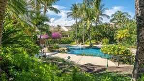 Una piscina rodeada de exuberante vegetación y palmeras, bajo un cielo despejado.