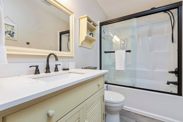 A modern bathroom with a white vanity, a large mirror, a glass shower enclosure, and a toilet.