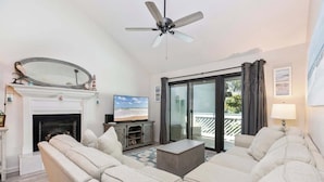 Una sala de estar con chimenea, televisor, ventilador de techo y balcón con vistas.