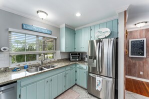 A kitchen with light blue cabinets, stainless steel appliances, a window with blinds, and a sign above the window.