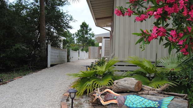 A pathway leading to a building with a wooden fence, surrounded by greenery and a decorative mermaid sculpture.