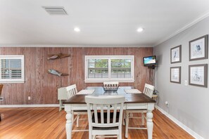 A dining room with a wooden paneled wall, a large window, and a television mounted on the wall.