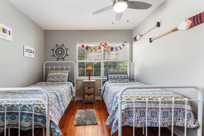 Ein Schlafzimmer mit zwei Betten, einem Deckenventilator, einem Fenster mit Jalousien und einer Wanduhr.