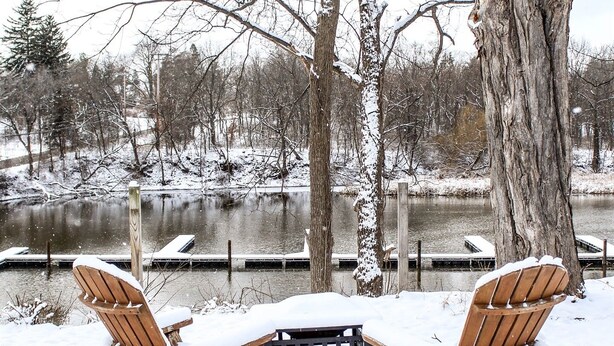 Zwei Adirondack-Stühle mit einem Holztisch in verschneiter Winterlandschaft.