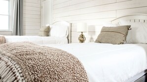 Ein Hotelzimmer mit zwei Betten, einem großen beigefarbenen Teppich, weißer Bettwäsche und einer Wand mit Holzpaneelen.