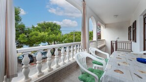 Un balcon avec des balustrades blanches, une table recouverte d’une nappe à motifs et des coussins verts.