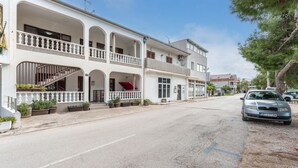 Un immeuble de deux étages doté d’un balcon, d’un escalier et d’une voiture garée dans la rue.
