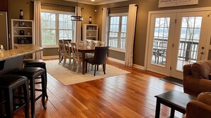 A spacious kitchen with a dining area, wooden flooring, and a view through large windows.