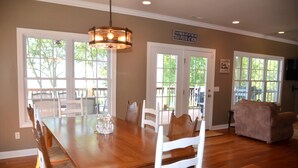 A dining area with a wooden table and white chairs, large windows, and a view of the outdoors.