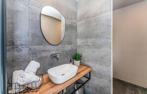 Een moderne badkamer met een grote, ovale spiegel, een witte wastafel, een kleine plant in pot en een handdoekrek.