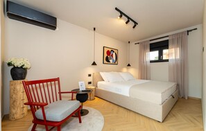 Een moderne slaapkamer met een bed, een rode stoel, een klein tafeltje, een bloemenvaas en een schilderij aan de muur.