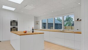 Una cocina moderna con armarios blancos, encimera de madera, horno integrado y un amplio ventanal con vistas al exterior.