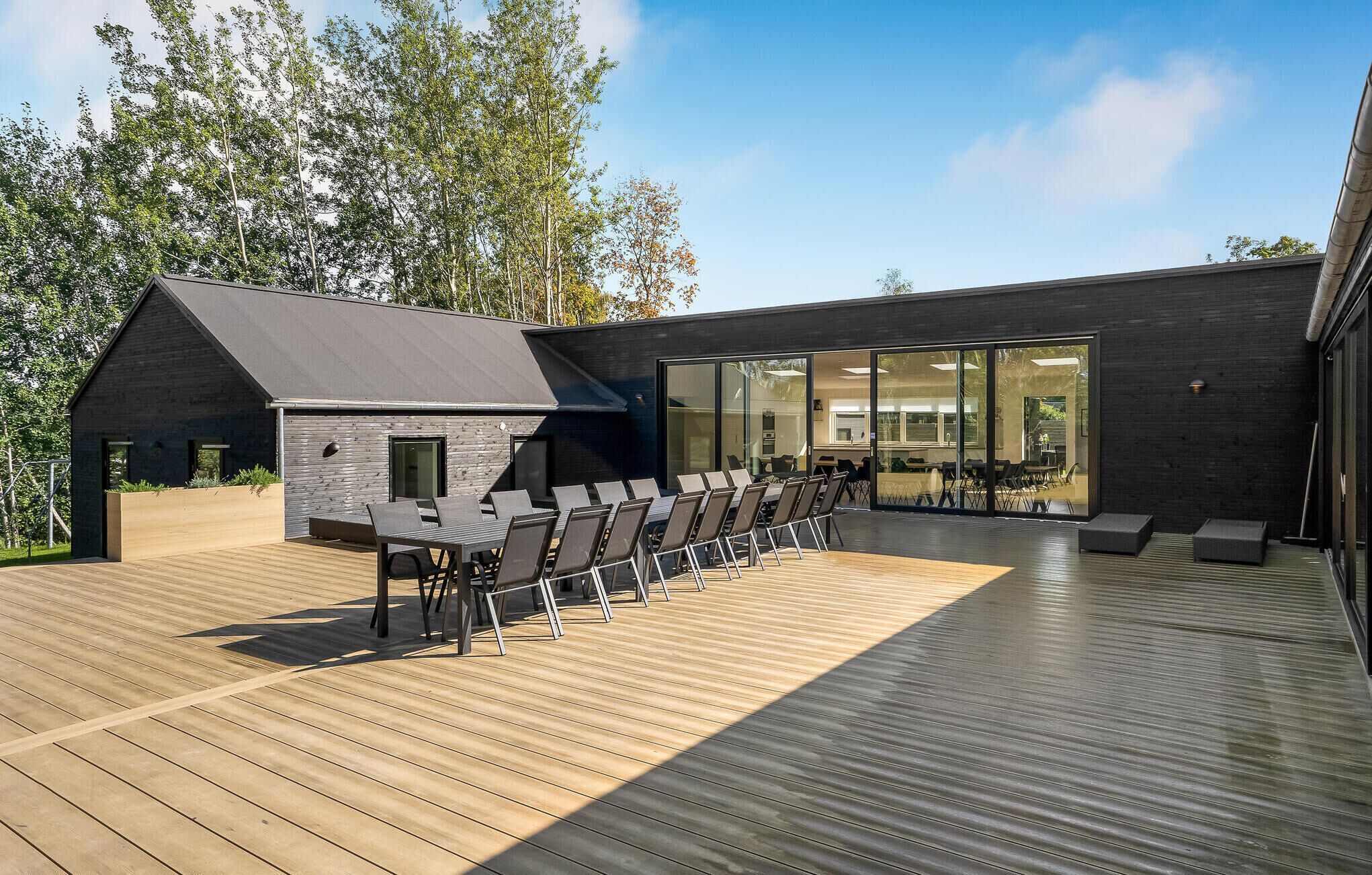 A modern building with a wooden deck, outdoor seating, and large glass windows.