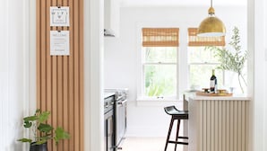 Une cuisine moderne dotée d’un îlot central, de stores verticaux en bois et d’un luminaire suspendu.