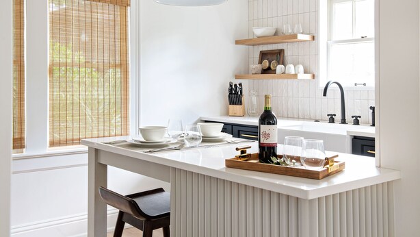 Une cuisine moderne dotée d’un îlot central, de meubles blancs et d’un luminaire suspendu.