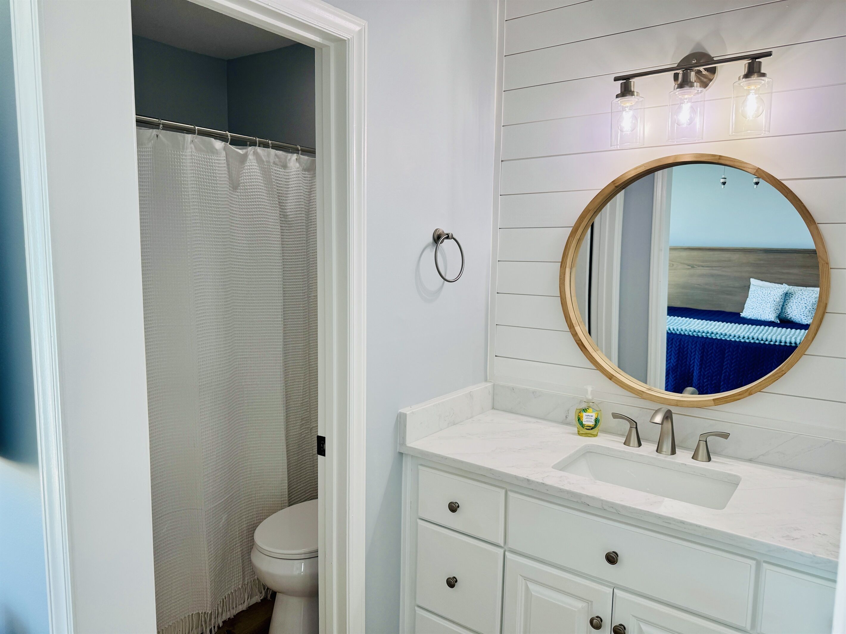 Une salle de bain avec un meuble-lavabo blanc, un miroir rond, des toilettes et un rideau de douche.