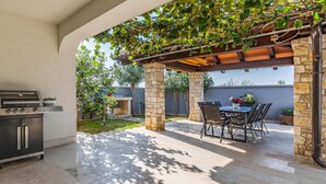 An outdoor patio with a grill, stone pillars, a pergola with climbing plants, and a table with chairs. - Gorgeous apartment in Medulin (Medulin)