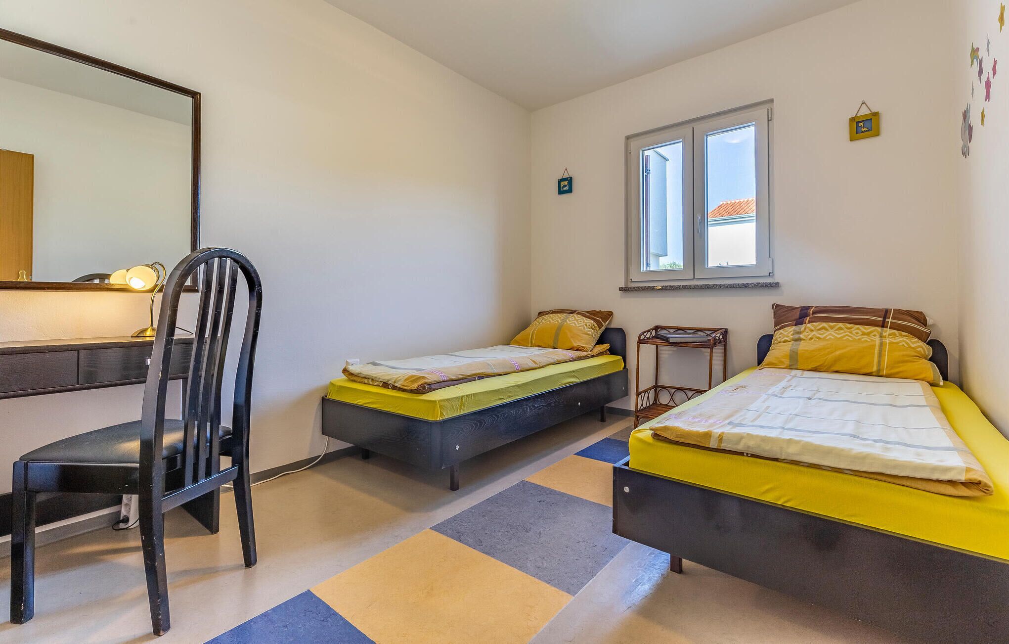 A bedroom with two single beds, a desk with a chair, a window, and a mirror.