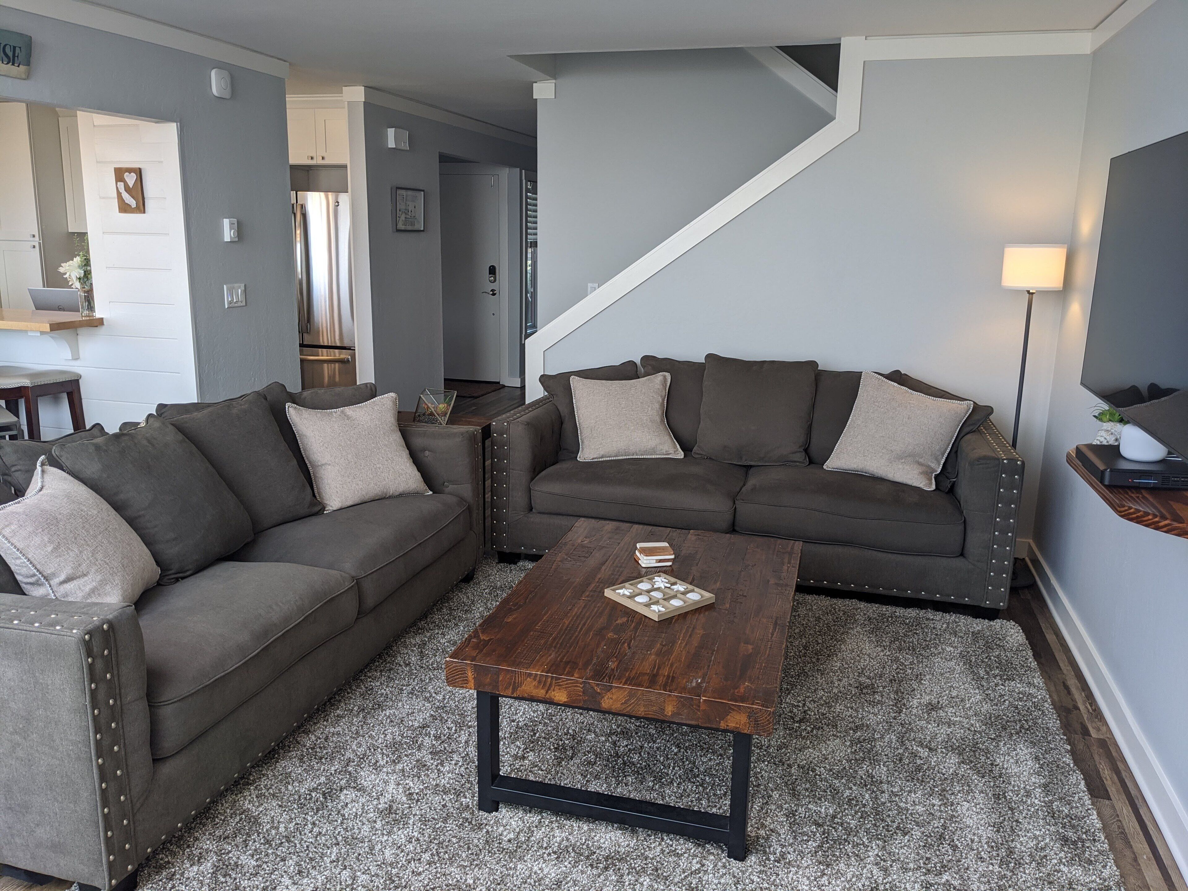 A modern living room with a gray sofa set, a wooden coffee table, and a staircase leading to another level.