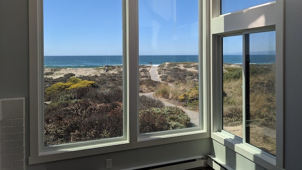 A room with a large window overlooking a coastal landscape with a clear sky.