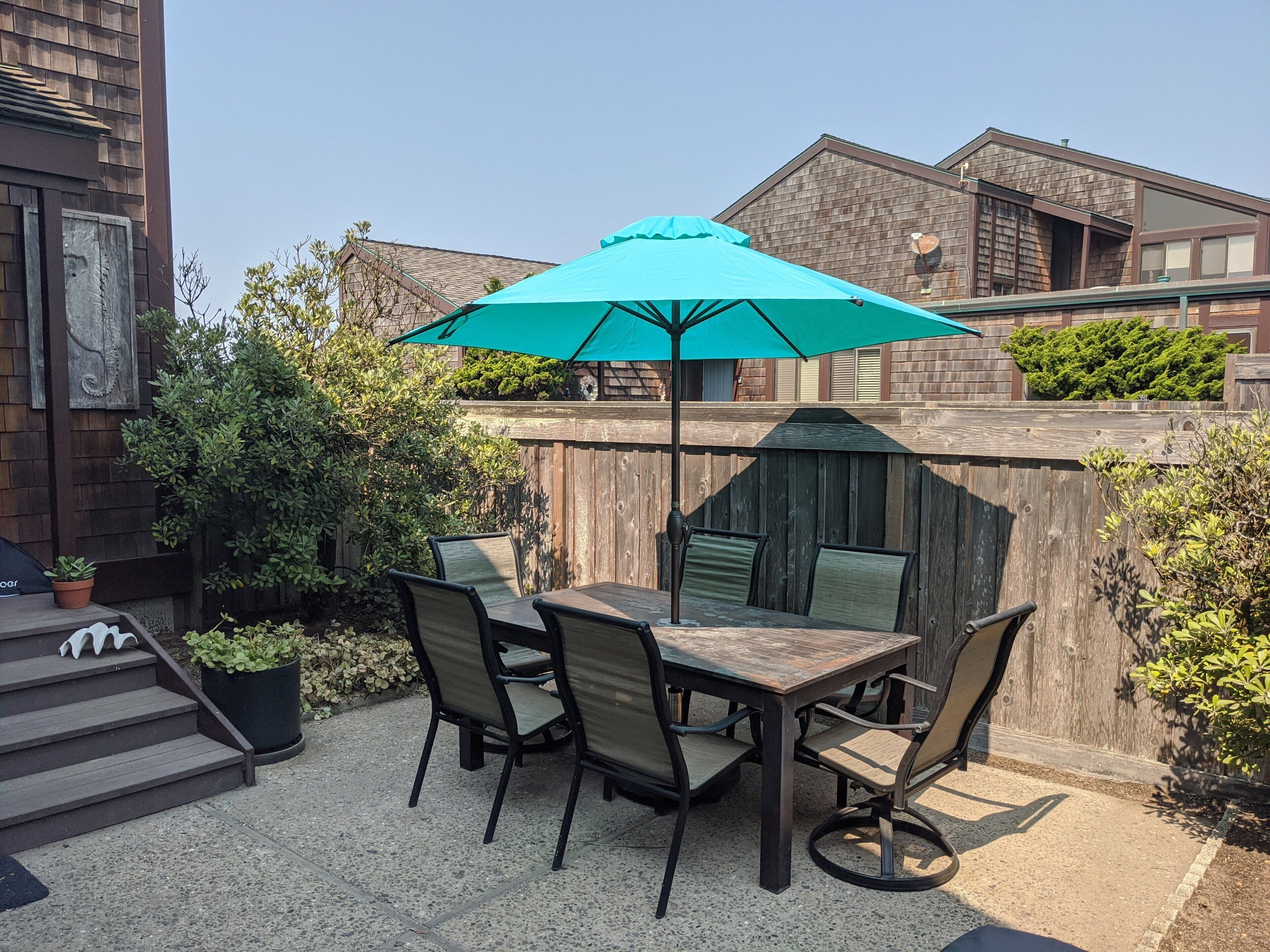 Une terrasse extérieure avec une table et des chaises en bois, un parasol turquoise et une clôture en bois.